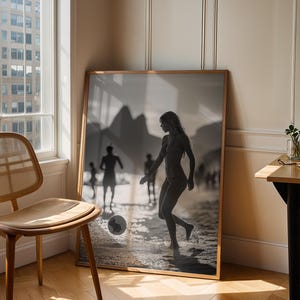 May include: A framed black and white photograph of a person playing soccer on a beach. The photograph is in a wooden frame and is leaning against a wall. A wooden chair and a small table are in the foreground.