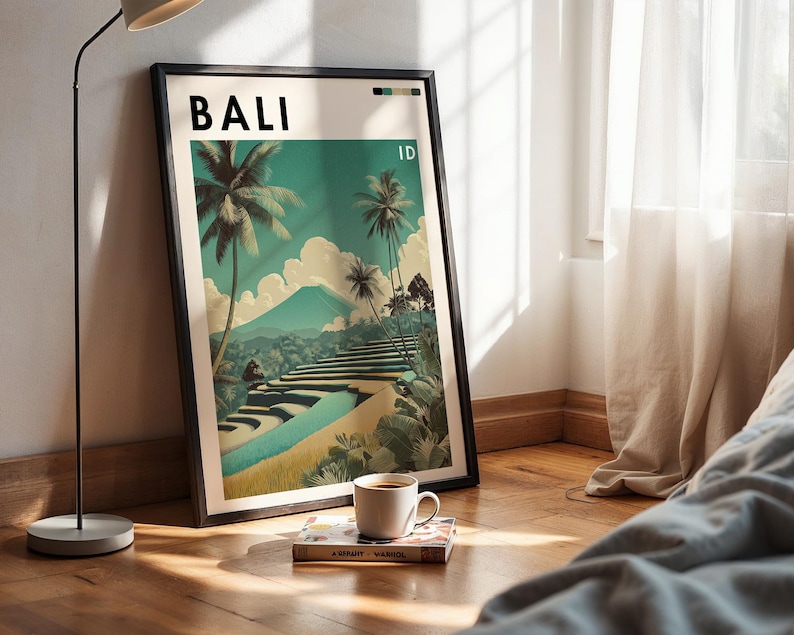 May include: A framed art print featuring a Bali landscape with palm trees, terraced rice fields, and a mountain. The print has the word "BALI" at the top. A coffee cup and a book rest on the wooden floor in front of the print.