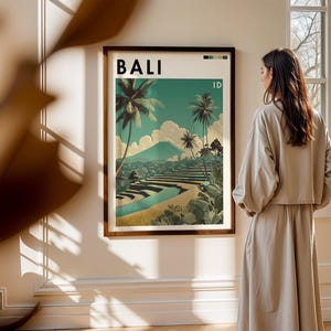 May include: A framed art print featuring a vintage travel poster design for Bali, Indonesia. The poster displays a scenic landscape with palm trees, terraced fields, and a mountain under a teal sky. The word "BALI" is at the top.