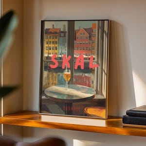 May include: Framed art print featuring a window view of colorful buildings and a glass of beer on a table. The word "SKAL" is written in pink letters across the top. The word "DANMARK" is written at the bottom.