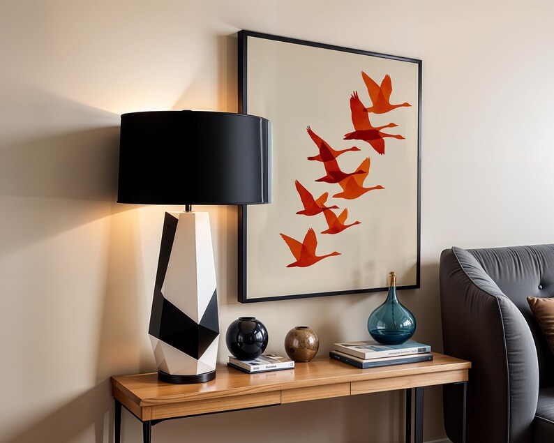 May include: A modern table lamp with a black lampshade and a geometric black and white base. A framed artwork with orange birds in flight hangs on the wall. Decorative spheres and a blue glass bottle sit on a wooden table.