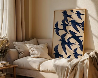 May include: A framed art print featuring a flock of navy blue birds in flight against a cream background. The artwork is displayed on a beige sofa with pillows and a blanket. The room has beige curtains and a wooden side table.