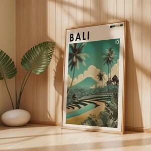 May include: A framed art print featuring a scenic illustration of Bali, Indonesia. The artwork showcases palm trees, terraced rice fields, and a mountain under a teal sky. The word "BALI" is printed at the top, with "ID" below it.