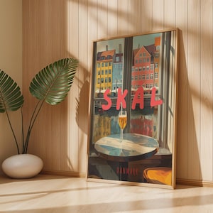 Pode incluir: Uma impressão artística emoldurada com uma cena urbana colorida com a palavra "SKAL" em letras vermelhas. Um copo de cerveja está em uma mesa em frente a uma janela. A palavra "DINAMARCA" está na parte inferior.