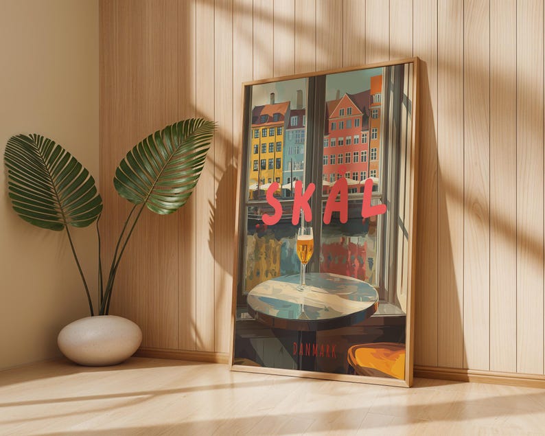 May include: A framed art print featuring a colorful cityscape scene with the word "SKAL" in red letters. A glass of beer sits on a table in front of a window. The word "DENMARK" is at the bottom.
