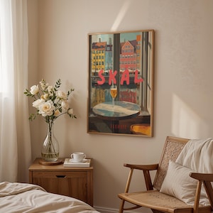 May include: A framed art print featuring a colorful cityscape with the word "SKAL" in red letters. A glass of beer sits on a table in front of a window. The print hangs above a wooden nightstand with a vase of white flowers.