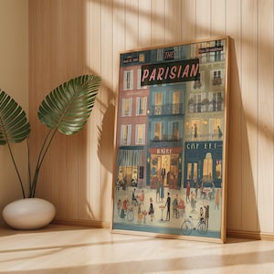 May include: A framed art print titled "The Parisian" depicts a bustling street scene with cafes, shops, and people. The artwork features colorful buildings, awnings, and figures, with bicycles and outdoor seating. The print is in a wooden frame and leans against a wall.