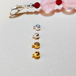 May include: A bracelet with large, translucent pink beads and small red accent beads. A silver clasp and several small silver and gold bead caps are also visible, likely for jewelry making.