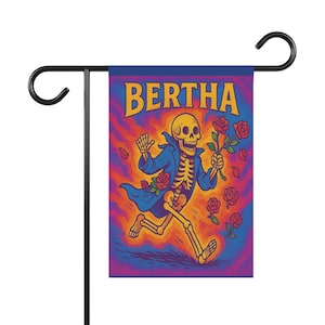 Puede incluir: Una bandera de jardín con un esqueleto corriendo con un abrigo azul, sosteniendo rosas. La palabra "BERTHA" está en amarillo encima del esqueleto. El fondo tiene un diseño psicodélico con tonos naranja, morado y azul. La bandera está montada en un soporte de metal negro.