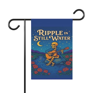 May include: A garden flag featuring a skeleton playing a guitar by a river under a starry night sky. The flag has the text "RIPPLE IN STILL WATER" and is decorated with roses. The flag is mounted on a black metal stand.