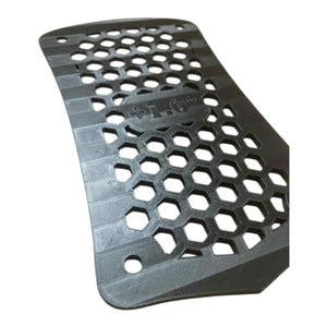 Peut inclure: Un objet rectangulaire noir et incurvé avec un motif en nid d'abeille et le texte "+1.0" visible. L'objet comporte une série de petits trous et est probablement un composant ou une partie d'un élément plus grand.