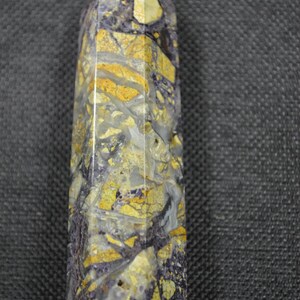 May include: A purple and yellow crystal point with a pointed tip. The crystal has a swirling pattern of purple and yellow.