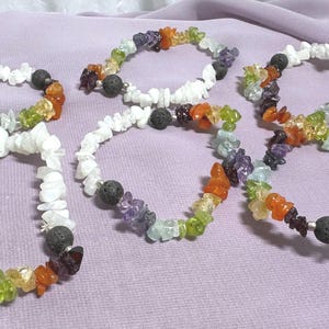 Puede incluir: Varios brazaletes de piedras preciosas con piedras blancas, negras y coloridas. Los brazaletes presentan una variedad de colores, incluyendo naranja, verde, morado y blanco. Cada brazalete tiene una piedra negra en el centro.