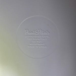 May include: A close-up of a white, circular design with the text "Paint & Petals" and care instructions: "Dishwasher Safe, Top Rack Only, Do Not Microwave, Made in China."