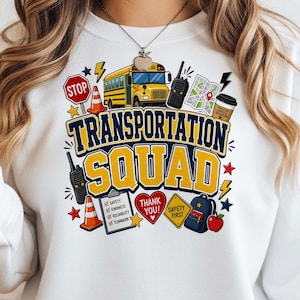 Puede incluir: Una sudadera blanca con un estampado gráfico que incluye el texto TRANSPORTATION SQUAD. El diseño muestra un autobús escolar amarillo, walkie-talkies, conos de tráfico, una señal de stop, un mapa, un café, una lista, un corazón y una mochila.