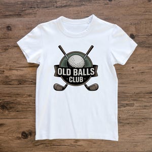 Puede incluir: Camiseta blanca con un dise&ntilde;o tem&aacute;tico de golf. El dise&ntilde;o incluye una pelota de golf, palos de golf cruzados y el texto "OLD BALLS CLUB" en un emblema circular. La camiseta est&aacute; hecha de un material suave.
