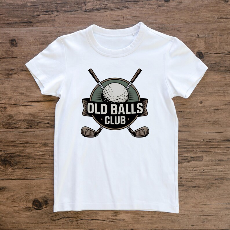 Puede incluir: Camiseta blanca con un dise&ntilde;o tem&aacute;tico de golf. El dise&ntilde;o incluye una pelota de golf, palos de golf cruzados y el texto "OLD BALLS CLUB" en un emblema circular. La camiseta est&aacute; hecha de un material suave.