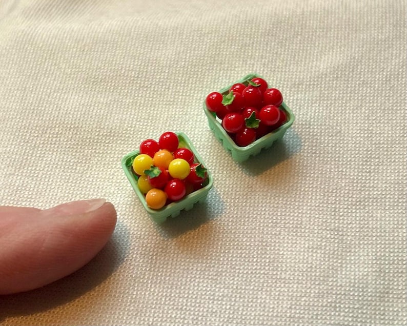 May include: Two miniature green plastic berry baskets filled with red, yellow, and orange berries. The berries have green leaves. The baskets are on a light beige textured surface.