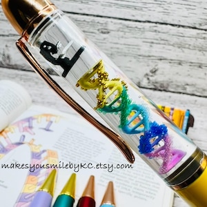 May include: A yellow and rose gold pen with a clear barrel containing a DNA model and a microscope. The pen has a gold tip and is next to pens with purple, green, red, and blue barrels.