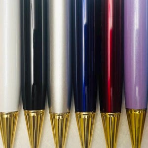 May include: A collection of colorful pens with gold-colored tips. The pens are arranged in a row, showcasing a variety of colors including yellow, pink, white, black, silver, blue, red, purple, teal, and magenta. The pens have a shiny finish.