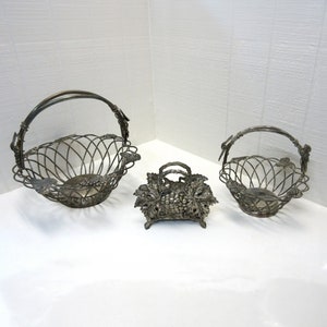May include: Set of three silver-tone wire baskets with grapevine designs. The baskets are in the shape of bowls with handles.