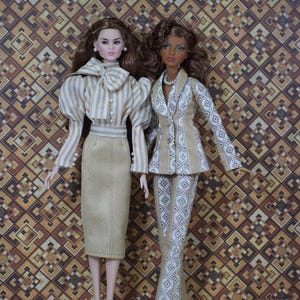 May include: Two fashion dolls are dressed in stylish outfits. One doll wears a tan pencil skirt and a striped blouse with a bow. The other doll is in a tan and white patterned pantsuit. The background is a brown and tan geometric pattern.