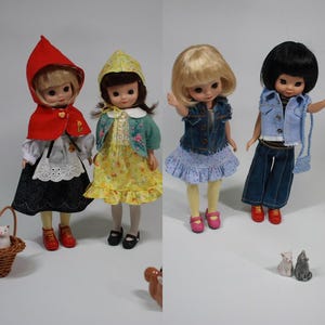 以下が含まれることがあります： さまざまな衣装を着た4体の人形。赤いフード付きケープと黒いスカートを着た人形。別の人形は、黄色の花柄のドレスと緑のジャケットを着ています。3番目の人形は、青いデニムベストとスカートを着ています。最後の人形はデニムベストとパンツを着ています。