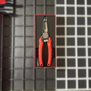 May include: Red and black wire strippers in a red-lined black box. The tool has a silver cutting head and red handles. The tool is designed for stripping wires and cables. The tool is likely used for electrical work.
