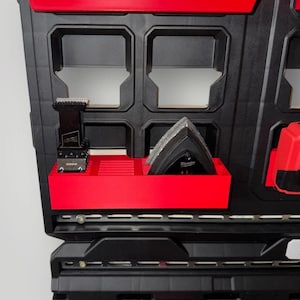 May include: A black and red tool organizer with multiple compartments. The organizer contains a saw blade and a multi-tool. The organizer is designed to hold various tools and accessories, providing a convenient storage solution.