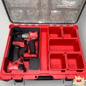 May include: A red Milwaukee Packout tool box with a clear lid, open to reveal two red and black power tools and several red storage compartments. The tools are a drill and an impact driver. The lid has the Milwaukee logo.