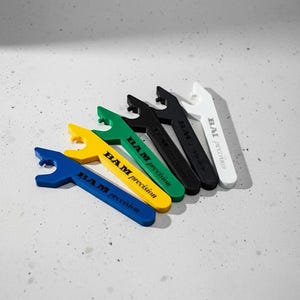 May include: An assortment of colorful bottle openers in blue, yellow, green, black, and white. Each opener has a wrench-like design with the text "BAM precision" printed on the handle. The openers are arranged on a light gray surface.