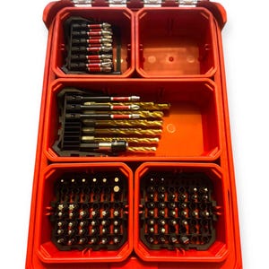 May include: A red plastic storage case with multiple compartments containing various metal drill bits and screwdriver bits. The top left section holds red-banded bits, the middle section holds gold drill bits, and the bottom sections hold assorted small bits.