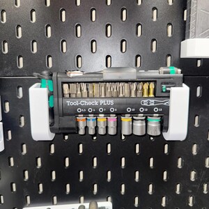 May include: A black Tool-Check PLUS set with various screwdriver bits and sockets. The set includes a ratchet handle and is held in white plastic holders against a black pegboard. The text "Tool-Check PLUS" is visible.