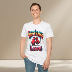May include: White t-shirt with a colorful graphic design that says "Stomping Out Bullying and Spreading Love". The graphic features boxing gloves and colorful paint splatters.
