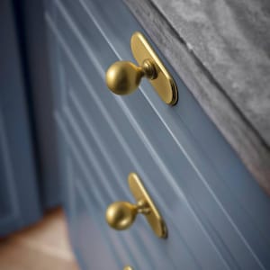 May include: Close-up of a blue cabinet with three gold-colored knobs. The knobs have a rounded shape and are mounted on rectangular backplates. The cabinet has a grooved design.