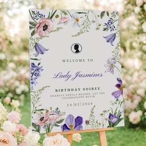 May include: A welcome sign for a birthday soiree, featuring floral accents and the text "Welcome to Lady Jasmines". The sign is displayed on a wooden easel amidst a garden setting with flowers.