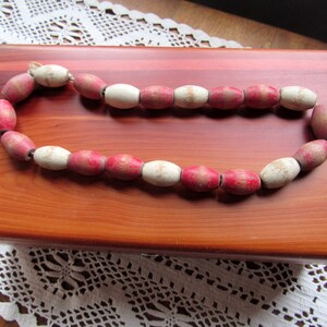 May include: A necklace made of wooden beads with alternating white and pink colors. The beads are oval shaped and have a natural wood finish.