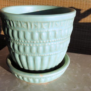 May include: A light blue ceramic planter with a textured design. The planter has a matching saucer.