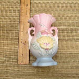 May include: A small, pink and blue ceramic vase with a floral design. The vase has two handles and a scalloped rim.
