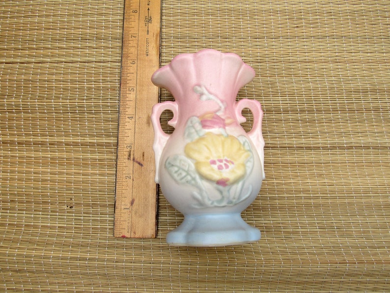 May include: A small, pink and blue ceramic vase with a floral design. The vase has two handles and a scalloped rim.