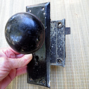 May include: Black antique door knob and lock set with a round knob and a keyhole. The lock is attached to a metal plate with screws.