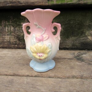 May include: A small, pink and blue ceramic vase with floral designs. The vase has two handles and a scalloped base.