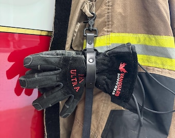 Puede incluir: Guantes de trabajo negros con texto rojo "MW ULTRA" y "VANGUARD SAFETY WEAR" colgando de una correa de cuero negro sujeta a una chaqueta ignífuga marrón. La chaqueta tiene rayas reflectantes amarillas y plateadas.