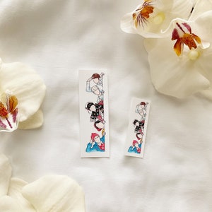 May include: Two white rectangular stickers with a watercolor illustration of people peeking from behind a wall. The stickers feature a line art style with pops of color, including red, blue, and black. The stickers are on a white background with white flowers.