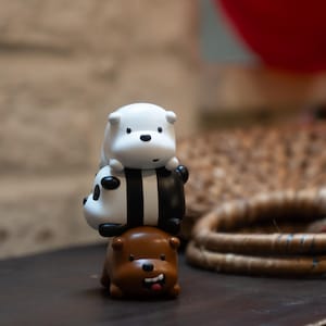 May include: A stack of three cartoon bear figurines. The bottom bear is brown with a smiling face and a red tongue. The middle bear is a panda with black and white markings. The top bear is white.
