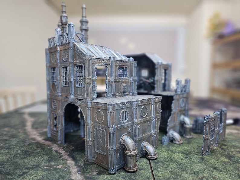 May include: A detailed miniature model of a futuristic industrial building, featuring multiple levels, arched doorways, and intricate pipework. The model is primarily gray with metallic accents, suggesting a weathered or aged appearance. Windows and architectural details are visible.