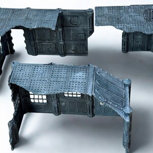 May include: A set of modular, gray-blue miniature building components. The pieces feature detailed industrial textures, including rivets, panels, and a distressed appearance. The set includes walls, roofs, and architectural elements for tabletop gaming.