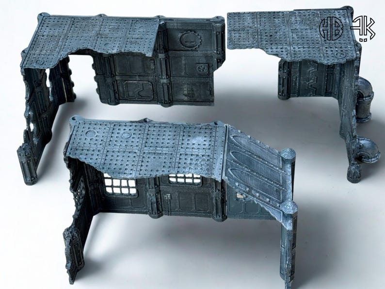 May include: A set of modular, gray-blue miniature building components. The pieces feature detailed industrial textures, including rivets, panels, and a distressed appearance. The set includes walls, roofs, and architectural elements for tabletop gaming.