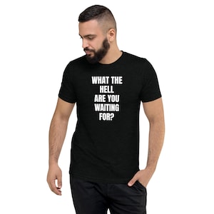 May include: Black t-shirt with the white text "WHAT THE HELL ARE YOU WAITING FOR?". The short-sleeved shirt is made of a soft material and is being worn by a person.
