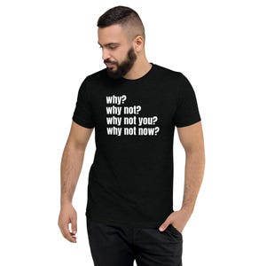 May include: Black t-shirt featuring the white text "why? why not? why not you? why not now?" The t-shirt is a crew neck design with short sleeves. The person in the image is wearing the t-shirt.